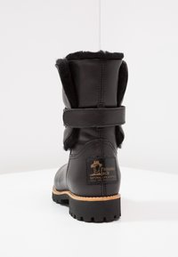 Botas de cuero negro con parte superior forrada de pelo y una correa. Marcado dorado notable en el tacón y suela de goma resistente con profundos relieves.