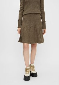 Bruin gebreid sweater en bijpassende rok met een rimpelzoom. De outfit wordt gecombineerd met chunky, crème-kleurige laarzen met zwarte zolen en gouden veters.