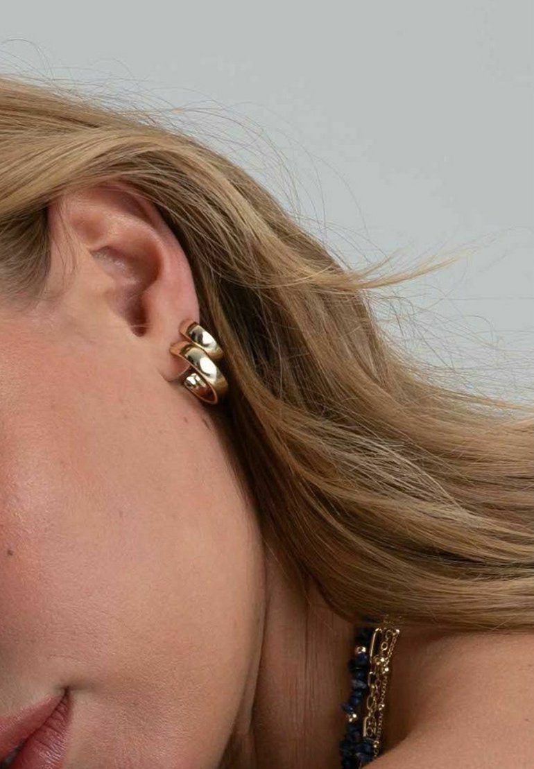 Guldpläterade hoopörhängen med en slät, glänsande yta. De har en vriden design som ligger tätt mot örsnibben.