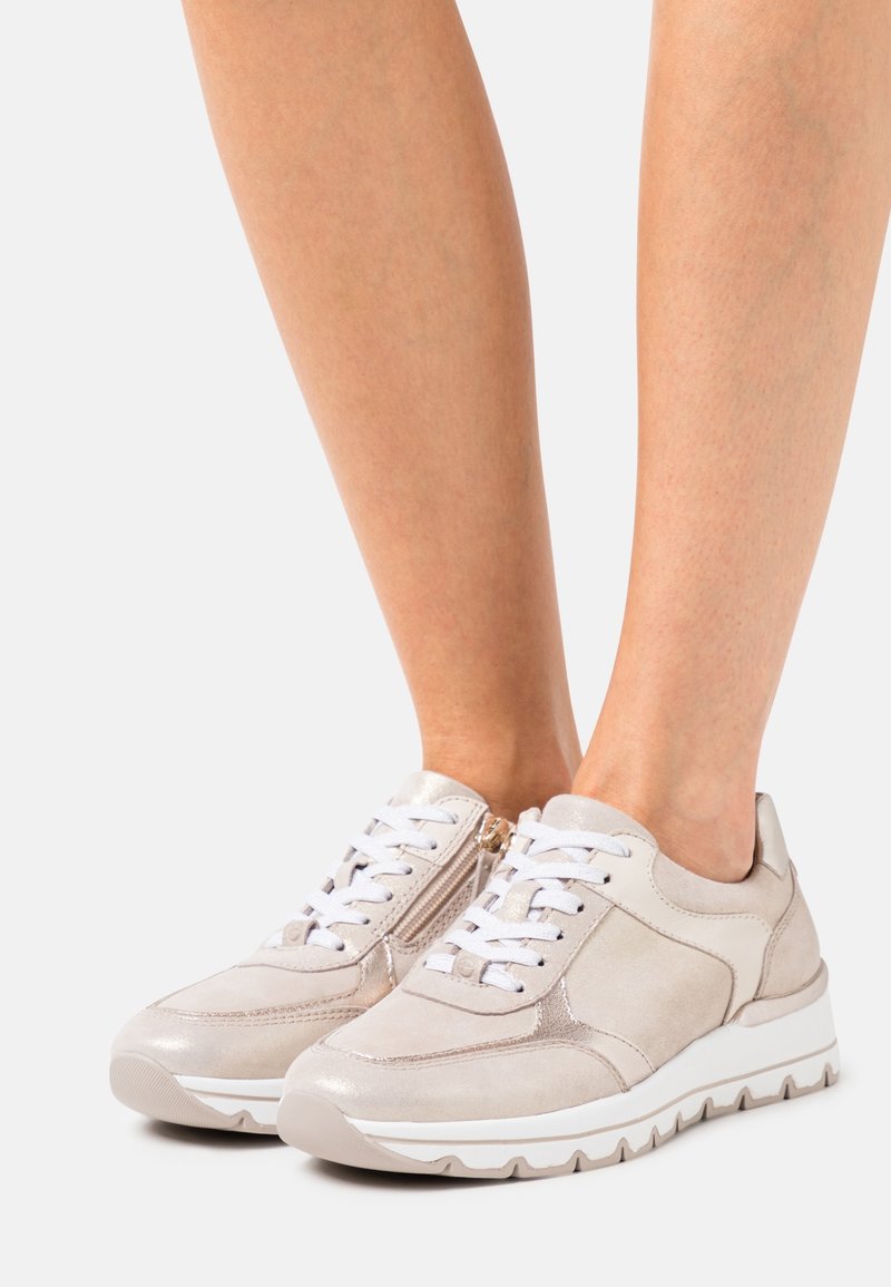 Baskets basses beige avec lacets blancs et fermeture éclair latérale portées pieds nus, vues de face et de profil sur fond blanc.