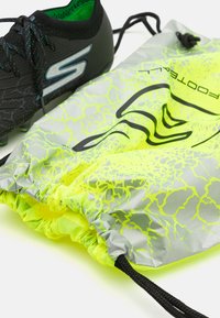 Sorte sportssko med teksturert overflate ved siden av en neon gul og grå snørsekk med grafisk mønster og svarte detaljer.