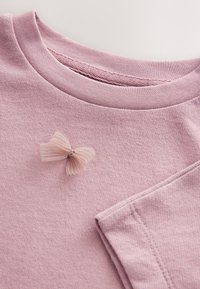 Lichtroze katoenen t-shirt met een ronde halslijn en korte mouwen. Voorzien van een geplooide strikaccent op de borst. Zachte, gestructureerde stof.