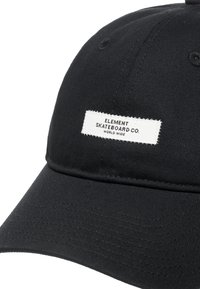 Svart tygkeps med en strukturerad krans och böjd skärm. Har en vit etikett med texten "ELEMENT SKATEBOARD CO." broderad på framsidan.