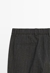 Pantaloni grigi a righe con un tessuto testurizzato, dotati di una vita e di una tasca posteriore, visti dall'alto su uno sfondo bianco.