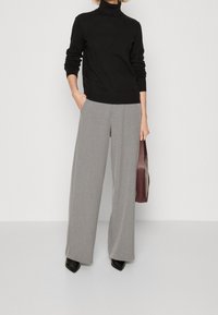 Maglione nero a collo alto abbinato a pantaloni grigi chiari a gamba larga, accentuato da una borsa bordeaux. Le scarpe presentano tacchi a punta neri.