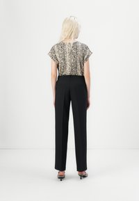 Cropped snake-patterned top in beige and black, paired with black high-waisted trousers. The model wears black heeled shoes.