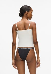 Biele tielko s tenkými ramienkami a priliehavým strihom, v kombinácii s čiernymi tangáčmi s bielym elastickým pásom s logom.