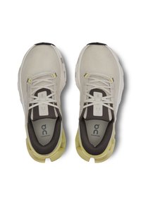 Baskets de course gris clair avec une tige en maille, accents gris foncé, semelle jaune et lacets plats. Présente un logo sur la languette et la semelle intérieure.