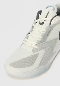 Witte sportieve schoen met bovenwerk van mesh, zilveren glittersAccent en gestructureerde grijze overlays. Kenmerkt veters en een doorschijnende, gevlekte zool.