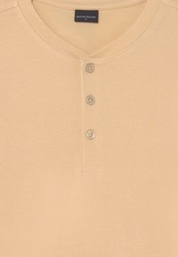 Camisa henley bege de manga curta em tecido suave com decote redondo e três botões na frente. Inclui detalhes de costura simples.