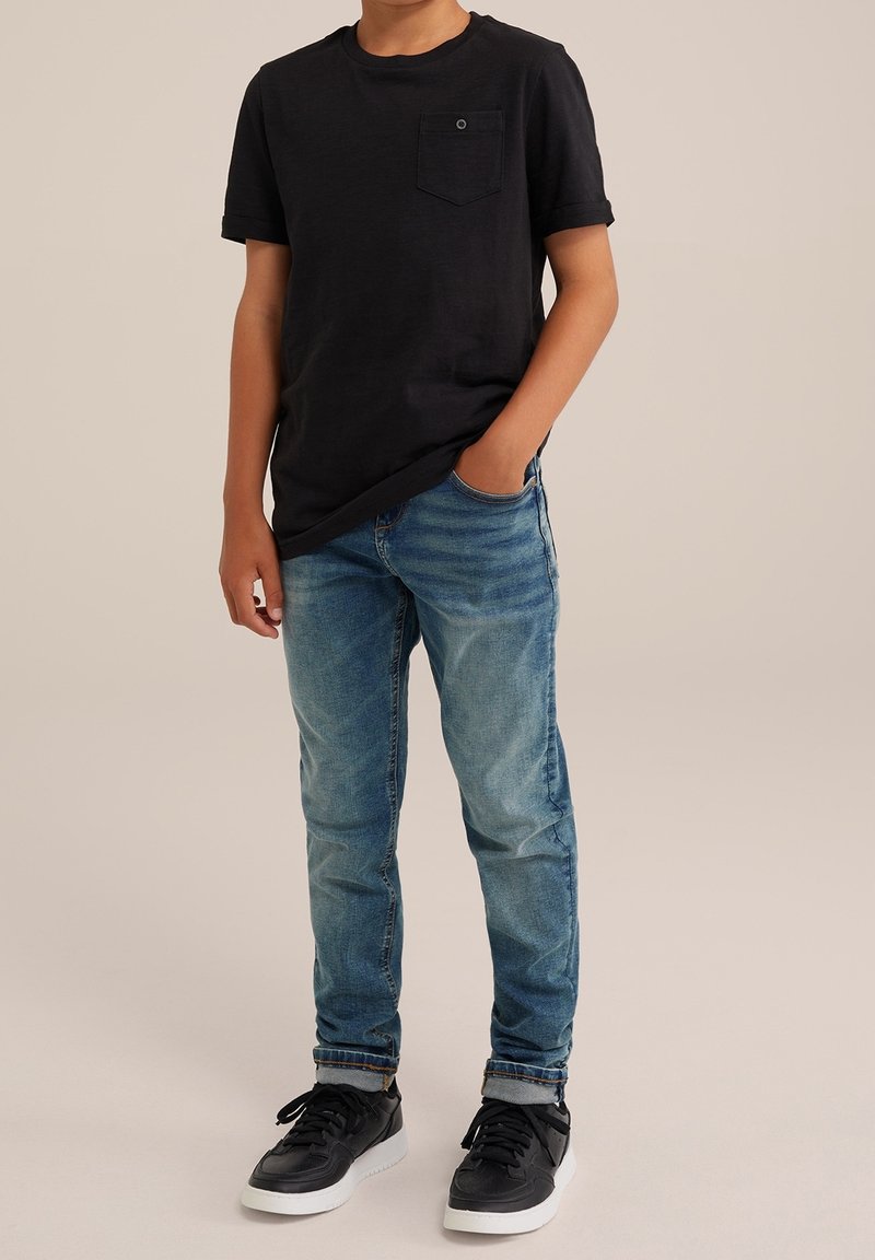 Svart kortärmad T-shirt med ficka, matchad med ljusblå denimjeans. Svarta sneakers med vita sulor.