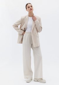 Béžový kostkovaný oversize blazer s jedním knoflíkem, kombinovaný s svetle béžovými širokými kalhotami. Nosit bílý tričko a robustní bílé boty.