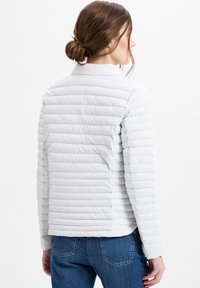 Leichte gesteppte Jacke in hellgrau mit horizontalen Nähten und hohem Kragen, kombiniert mit blauen Jeans.