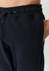 Pantalones de chándal azul marino con una tela texturizada, cinturilla elástica y cordón. Cuenta con bolsillos laterales y un diseño de corte relajado.