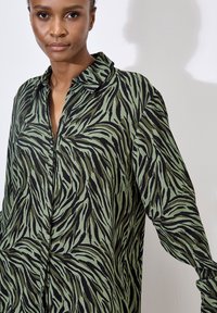 Long-sleeve shirt featuring a green and black zebra-stripe pattern, made from a lightweight fabric with button details and a collared neckline.