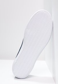 Vit gummisula med ett zigzag-mönster; mörk tygovandel synlig längs kanten, vilket visar en minimalistisk design.