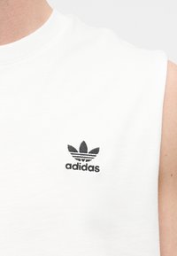 Κοντινή εικόνα λευκού αμάνικου με μαύρο κεντημένο λογότυπο Adidas trefoil στο στήθος.