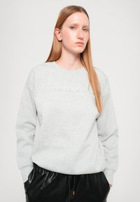 Sivá mikina s kulatým výstrihom a textúrovaným logom "MICHAEL KORS" na hrudi; doplnená o čierne plisované kožené nohavice.