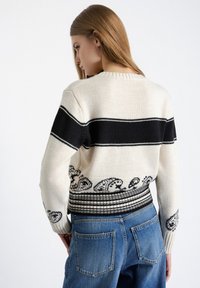 Maglione lavorato a maglia con base crema, caratterizzato da una striscia nera sul petto e una banda decorata bianca e nera all'orlo.