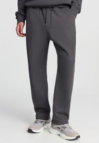 Szare dresy wykonane z miękkiego materiału, z elastycznym paskiem w talii i sznurkiem do regulacji, o luźnym kroju. Połączone z szarymi butami sportowymi.