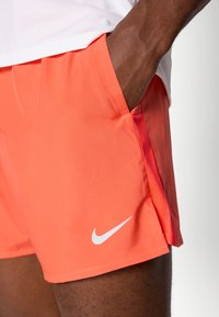 Nike-shortsit elävässä korallinvärissä, valmistettu keveästä kankaasta. Varustettu sivutaskulla ja valkoisella logovärityksellä. Sileä pinta, jossa on verkkokangsiraidat.