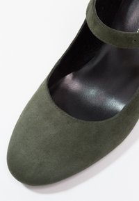 Chaussure Mary Jane en daim vert foncé avec embout arrondi et semelle intérieure noire sur fond blanc.
