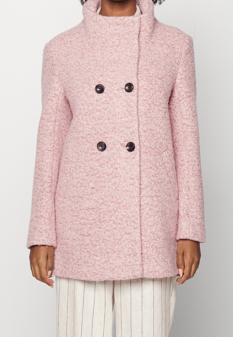 Dvouřadový růžový vlněný kabát s texturovanou látkou, který má velké černé knoflíky a vysoký límec. Dlouhé rukávy a rovný střih.