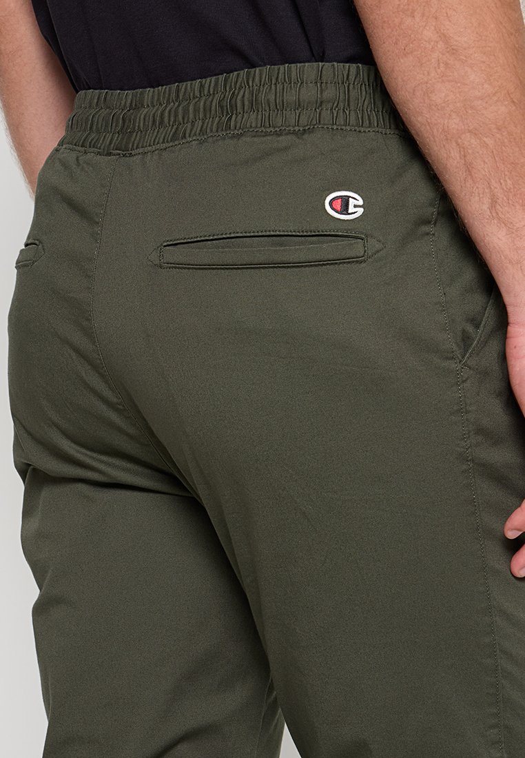 Un pantalon de sport vert avec une taille élastique, deux poches latérales et un petit logo brodé dans le dos. Texture lisse et design ajusté.
