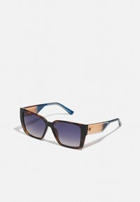 Occhiali da sole con gradiente nero e marrone, lenti rettangolari, astine in acetato blu e un logo metallico GUESS sulle tempie.