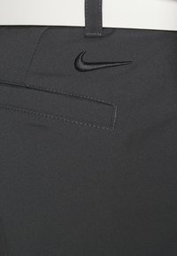 Sorte treningsbukser i glatt, teksturert stoff. Har en svart Nike-logo og en liten lomme detalj nær midjen.