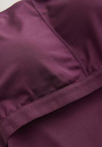 Gros plan d’un tissu lisse mauve profond avec des coutures visibles et une bande horizontale d’une texture légèrement différente.