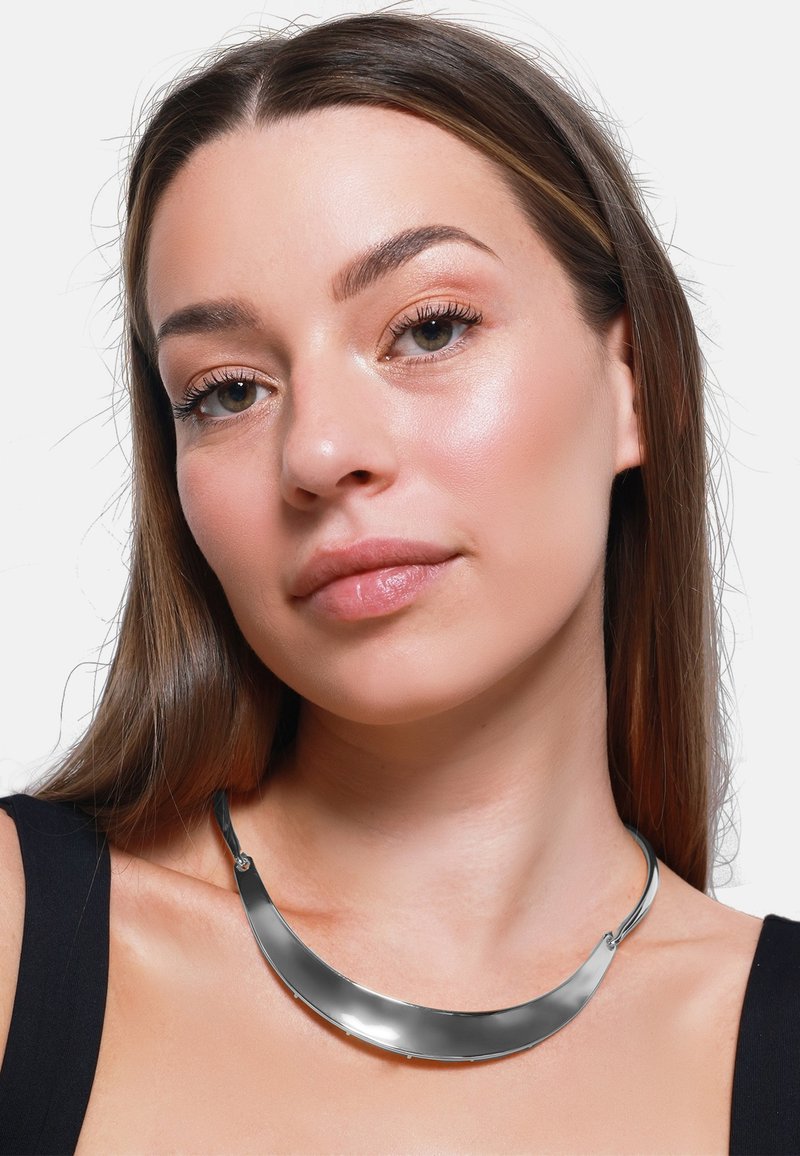 Collier en métal avec un design lisse et courbé en argent brillant, présentant une finition élégante et des accents minimalistes pour un look contemporain.
