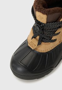 Braun und schwarze Winterstiefel mit einem weichen Futter, ausgestattet mit einem Schnellverschluss-System und einer strukturierten Gummisohle, auf einer hellen Fläche platziert.