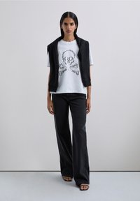White t-shirt with a black skull and crossbones graphic, paired with loose-fitting black wide-leg pants and a sleeveless black vest.