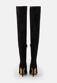 Botas negras por encima de la rodilla en suave ante. Punta afilada, tacón de aguja, cierre de cremallera lateral y textura suave. Diseño clásico y de alta calidad.