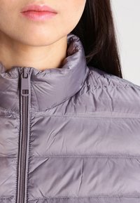 Jasnofioletowa kurtka puchowa z wysokim kołnierzem, pionowym pikowaniem i zamkiem błyskawicznym z przodu, o gładkiej, błyszczącej fakturze.
