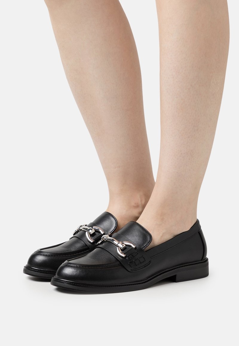 Mocassins en cuir noir avec un détail de chaîne en argent brillant sur le devant, dotées d'un bout rond et d'un talon plat. Texture lisse, design classique.