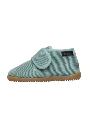Chaussures en velours côtelé vert avec une sangle velcro et une semelle en caoutchouc. Présente des rayures texturées et une étiquette noire sur le talon.