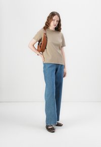Beige kortermet t-skjorte kombinert med vide blå jeans og sko med leopardmønster. Brun veske henger fra skulderen, flat tekstur generelt.