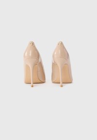 Beige patent leather high heels with a pointed toe, stiletto heel, and gold logo detail at the back. Smooth, shiny finish.