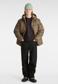Brun pufferjakke med hætte, sorte jeans og sorte sko. Mintgrøn strikket hue og enkel sort t-shirt under.
