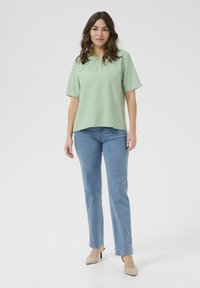 Top verde chiaro a maniche corte con scollatura rotonda, tessuto testurizzato, abbinato a jeans dritti blu medio e tacchi beige.