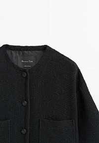 Mustassa tekotäytteessä oleva neuletakki, jossa on pyöreä kaula-aukko, kaksi etutaskua ja suuret mustat napit. Tunnusmerkki lukee "Massimo Dutti."