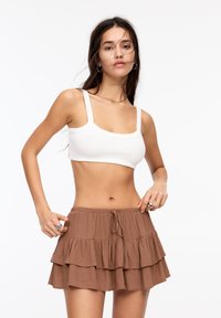 Wit geribbelde crop top met dunne banden, gecombineerd met een bruine gelaagde miniskirt met ruffles en een verstelbare trekkoord taille.