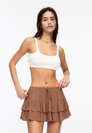 Vit ribbad crop-top med tunna axelremmar, parat med en brun flikskjol i mini-längd med volanger och justerbart snörliv.