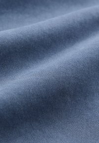 Denim fabric in a medium blue shade, featuring a smooth, textured surface with fine, vertical ridges, showcasing quality material details.