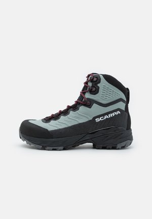 Wanderstiefel mit einem Obermaterial aus grauem und schwarzem Textil, einer Gummikappe an der Zehe, roten Schnürsenkeln und strukturierten Akzenten. Auffälliges Profil der Sohle.