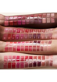 Vier Arme mit unterschiedlichen Hauttönen zeigen mehrere Farbmuster glänzender Lippenstiftfarben von Pink- und Rottönen bis hin zu Nudetönen.