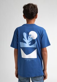 Camiseta de algodón azul con un audaz diseño abstracto en blanco y azul claro en la parte posterior, con cuello redondo y mangas cortas.