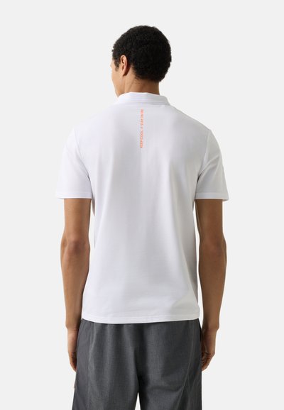 Man wearing plain white short-sleeve polo shirt with small vertical orange text "KEEP COOL / STAY ON FIRE" on upper back, paired with dark gray shorts.